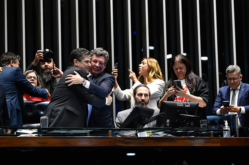 Reginaldo Lopes abraça Davi Alcolumbre na mesa do Senado, acompanhado por parlamentares.